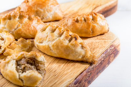 Hot pasties from butter enriched puff pastry filled with minced beef, potato, onions and swede on the wooden chopping boardの写真素材