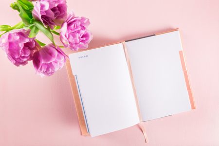 Open Notebook for writing down plans or dreams, girly settings on the table with bunch of tulips and pink backgroundの写真素材