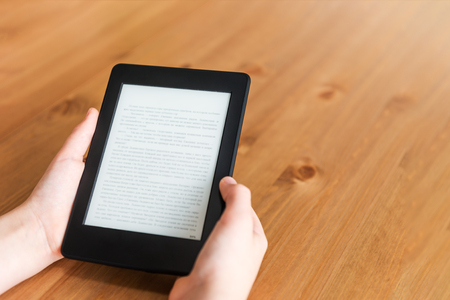 Girl is reading ebook on digital tablet device while sitting at the tableの写真素材