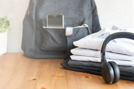 Back to school concept, backpack with school uniform such as white shirts and sweater, as well as electronic devices such as smart watch, mobile phone and headphones on the light background, toned imageの写真素材