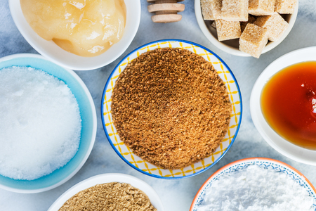 Different Kinds of Sugar and Sweeteners in the Bowls, such as coconut, pure cane, icing, maple syrup, dark brown soft sugar, honey, demerara cubesの写真素材