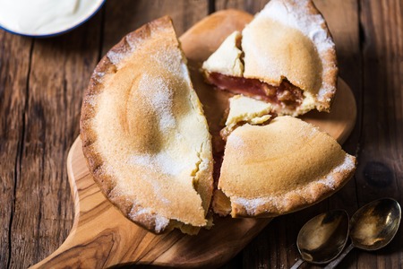 Piece of fresh rhubarb and strawberry pie with cream nearby, rustic wooden background