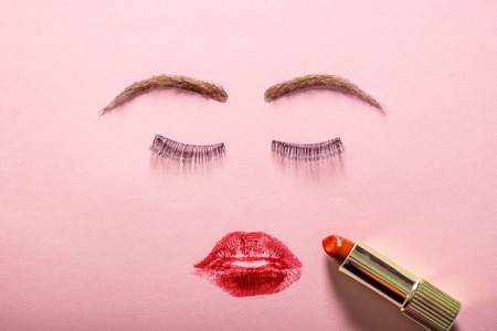 Creative woman face made of eyelashes, wig eyebrows and red lipstick stains as lips. Minimal beauty concept. Hair loss products. Pink backgroung, fashion flat layの写真素材