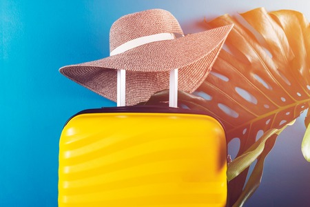 Bright and stylish cabin size suitcase with straw hat and monstera leafの写真素材
