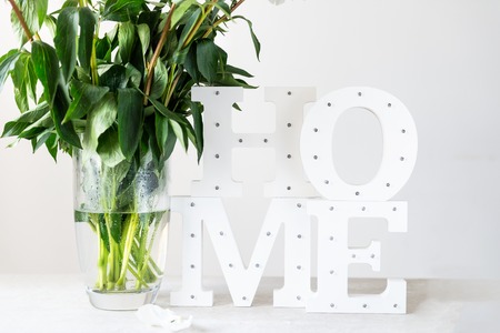 Bunch of amazing peonies in the vase and wooden letters HOME with white wall background