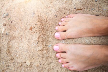 Young lady is showing her light pink pedicure nails on sandy beach backgroungの写真素材