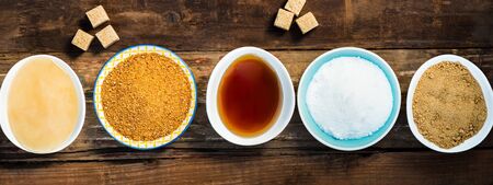 Different Kinds of Sugar and Sweeteners in the Bowls, such as coconut, pure cane, icing, maple syrup, dark brown soft sugar, honey, demerara cubesの写真素材