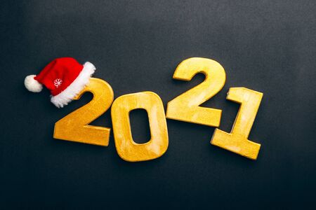 Happy New Year 2021. Golden digits 2021 with christmas hat are on black background. Holiday Party Decoration or postcard concept with top view and copy space.の写真素材