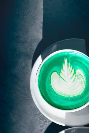 Cup of green matcha latte in the cafe, nice sunny day, shadows on the tableの写真素材