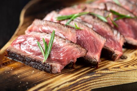 Juicy Beef Rib Eye Steak slices slightly salted, with herbs and spices on wooden board. Dark black backgroundの写真素材