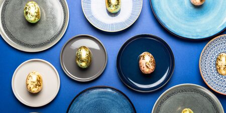 Different Ceramic Plates with Golden Speckled Easter Eggs of pastel colors on blue background. Happy...