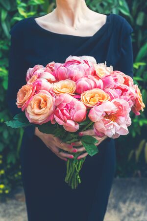 Woman in black dress is holding bunch of pink peonies and roses. Card Concept, pastel colors of flowersの写真素材