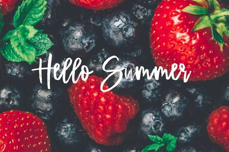 Fresh summer berries such as blueberries, strawberries, raspberries with Hello Summer text, top view