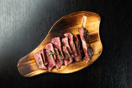 Juicy Beef Rib Eye Steak slices slightly salted, with herbs and spices on wooden board. Dark black background, top view