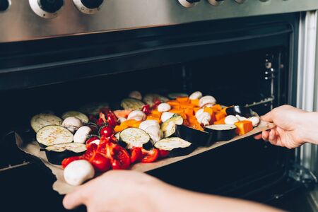 Woman hands placing raw vegetables on tray to the oven for roasting. Healthy Detox Dinner from aubergine, red pepper, cherry tomatoes, butternut squashの写真素材