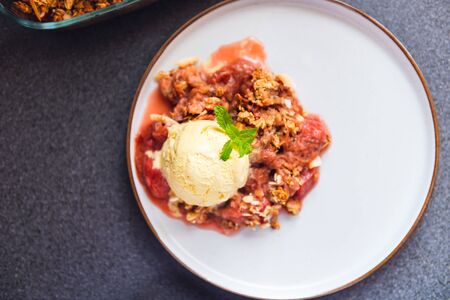 Home cooked Rhubarb and Strawberry crumble from oatmeal and nuts topping and with vanilla ice cream scoopsの写真素材