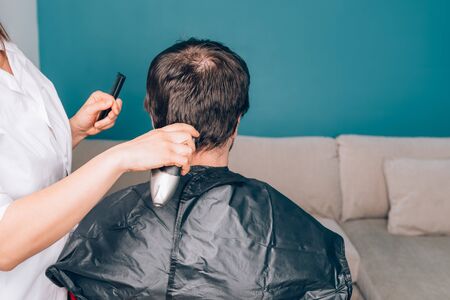 Wife is cutting her husbands hair with the trimmer in the living room during lock down. Stay at home conceptの写真素材