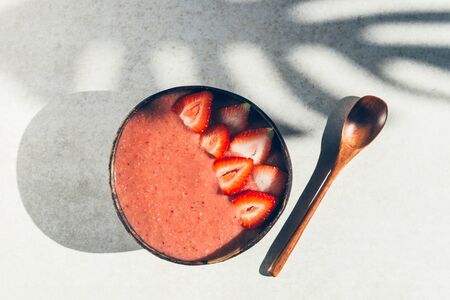 Pink Smoothie from Banana and Strawberries with pieces of Strawberries in the Coconut Shell Bowl, strong shadows. Healthy summer breakfastの写真素材