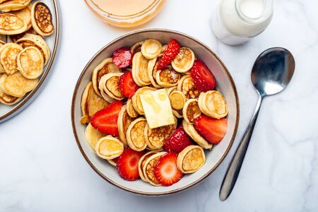 Trendy home breakfast with tiny cereal pancakes with piece of butter and fresh strawberries in the...