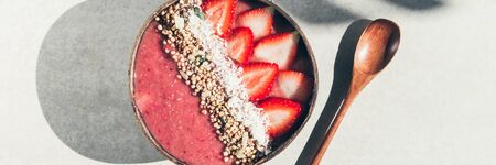 Pink Smoothie from Banana and Strawberries with pieces of Strawberries, Granola and Coconut Shreds on top in Coconut Shell Bowl, strong shadows. Healthy summer breakfast, top viewの写真素材
