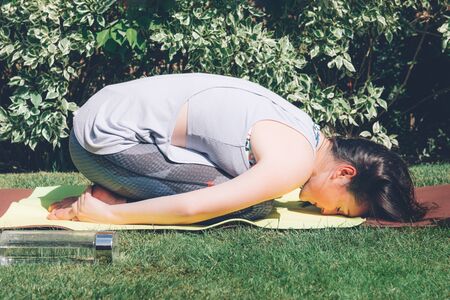 Happy woman is doing online yoga with smartphone on tripod during self isolation at her garden, no...