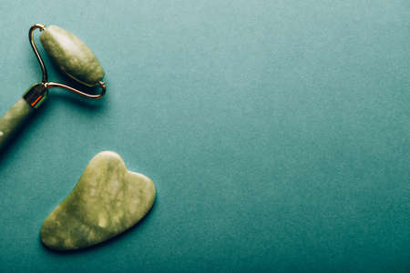 Jade face roller and Gua sha stone for beauty facial massage therapy on green backgroundの写真素材