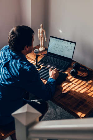 Young university professor is doing online lecture for his students from home during lockdown. He is...