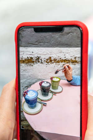 Woman is doing photos on her smartphone of Butterfly Matcha from blue matcha and nut milk, Rose Matcha from green tea powder infused with rose water, Black Latte from activated charcoal, date syrupの写真素材