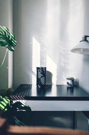 Simple home office with small table and wireless speaker, strong shadows from the windowの写真素材
