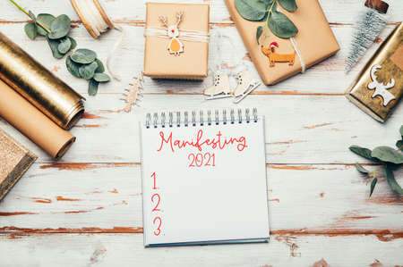 Empty open notebook for writing xmas wishes and with word Manifesting 2021. Gifts wrapped in...