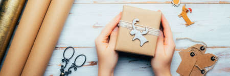 Hands are holding gift, wrapped in recycled brown paper with handmade toppers , christmas background...