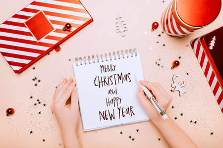 Hands writting with words Merry Christmas and Happy New Year. Reusable Red and white boxes for presents in different shapes, gift wrapping and preparation for the festive Christmas holidays seasonの写真素材