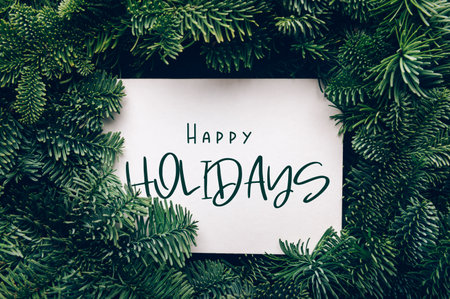 Happy holidays text, card concept. Holiday background with white card in the middle of evergreen tree branches, christmas and festive season idea, minimalistic designの写真素材