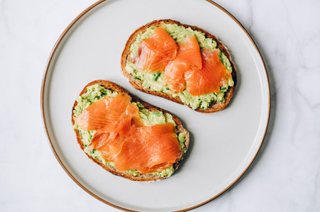 Toasted bread with mashed avocado and smoked salmon on grey plateの写真素材