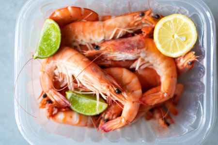 Ocean king prawns or jumbo shrimps with lemon in plastic box slices on grey backgroundの写真素材