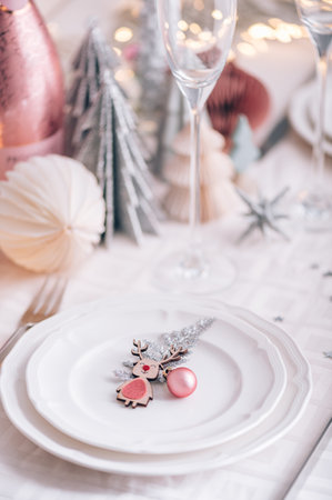 Xmas table settings in white and pink colors with christmas trees on background, empty plates and glasses ready for festive dinner and partyの写真素材