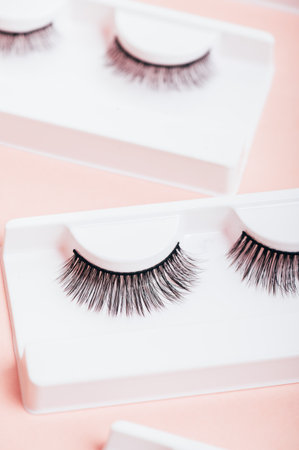 Different fake eyelashes in boxes on trendy pastel pink background. Makeup accessories and beauty...