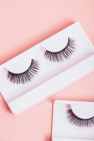 Different fake eyelashes in boxes on trendy pastel pink background. Makeup accessories and beauty cosmetics products for women. Top view, flat lay.の写真素材