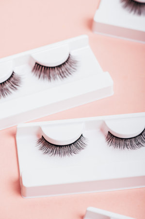 Different fake eyelashes in boxes on trendy pastel pink background. Makeup accessories and beauty cosmetics products for women. Top view, flat lay.の写真素材