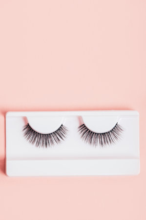 Different fake eyelashes in boxes on trendy pastel pink background. Makeup accessories. cosmetics...