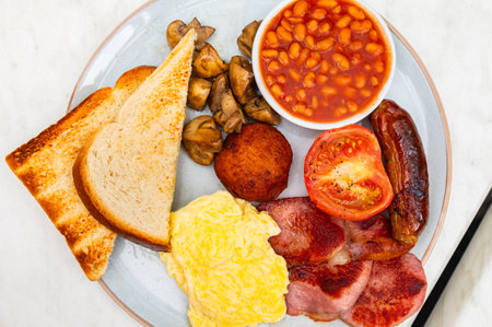 Full English Breakfast with sausage, mushrooms, tomato, bacon, homemade hash brown, baked beans, scrambled eggs and toast bread with butterの写真素材