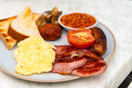 Full English Breakfast with sausage, mushrooms, tomato, bacon, homemade hash brown, baked beans, scrambled eggs and toast bread with butterの写真素材