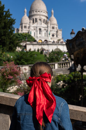 Tourist Girl with red bow in her hair is watching Basilica of Sacre Coeur de Montmartre, commonly known as Sacre-Coeur Basilica, in Parisの写真素材