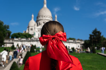 Tourist Girl with red bow in her hair is watching Basilica of Sacre Coeur de Montmartre, commonly known as Sacre-Coeur Basilica, in Parisの写真素材