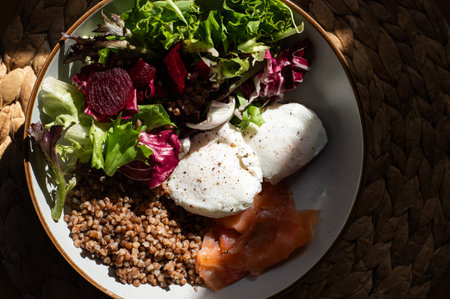 Homemade healthy and balanced breakfast from buckwheat, smoked salmon, salad leaves, beetroot, and poached eggs. Breakfast with strong sun light and shadowsの写真素材