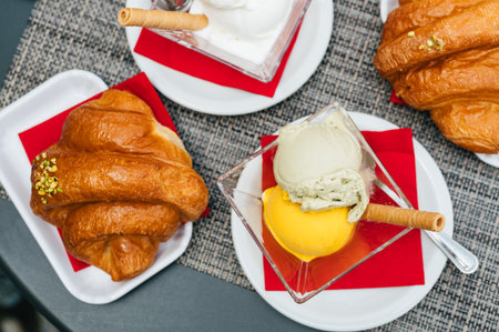 Italian coffee break in cafe during holiday season with pistachio and mango scoops of gelato with freshly baked croissantsの写真素材