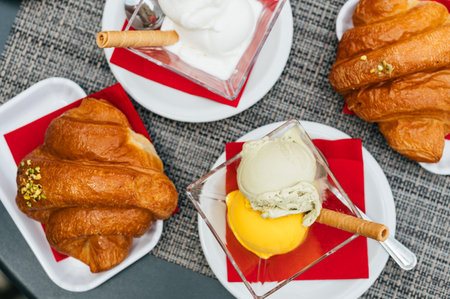 Italian coffee break in cafe during holiday season with pistachio and mango scoops of gelato with freshly baked croissantsの写真素材