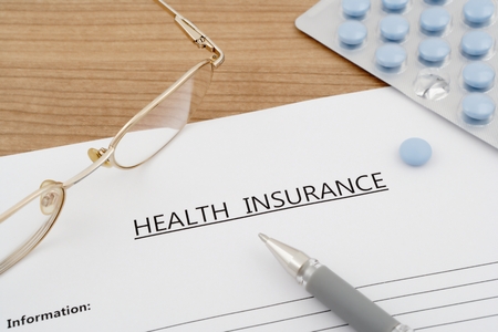 health insurance document with pills eyeglasses on wooden tableの写真素材
