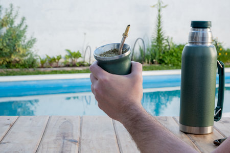 Young man drinking mate in the morning in front of the pool.