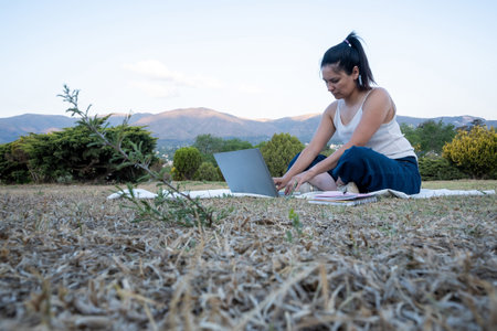Latina girl went to a beautiful park where you can see mountains in the background, accompanied by her notebook and cell phone, to be able to do her work.の写真素材